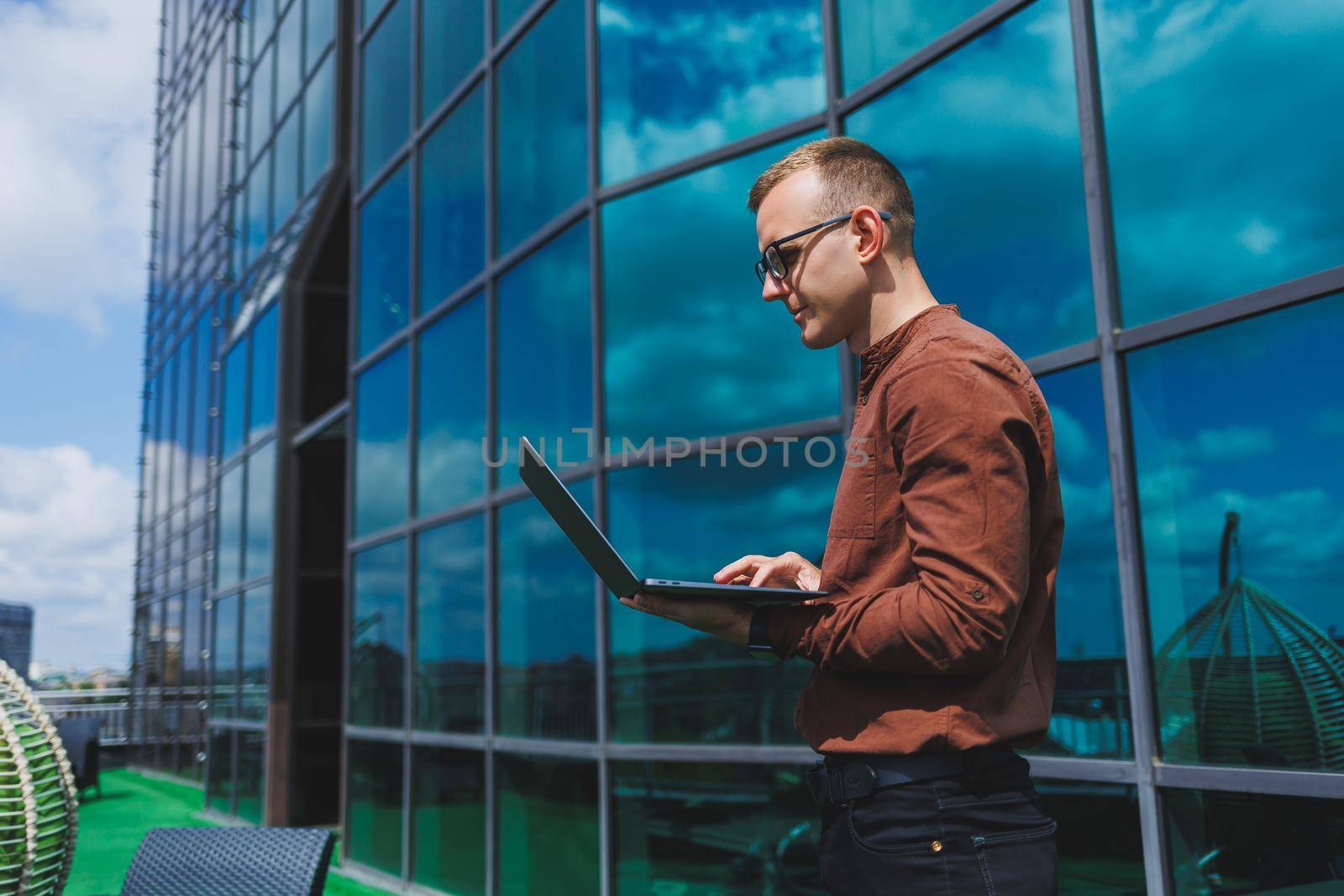 Cheerful businessman, formally dressed, pleased with received good news about contract details, sitting on office terrace with laptop, successful male entrepreneur