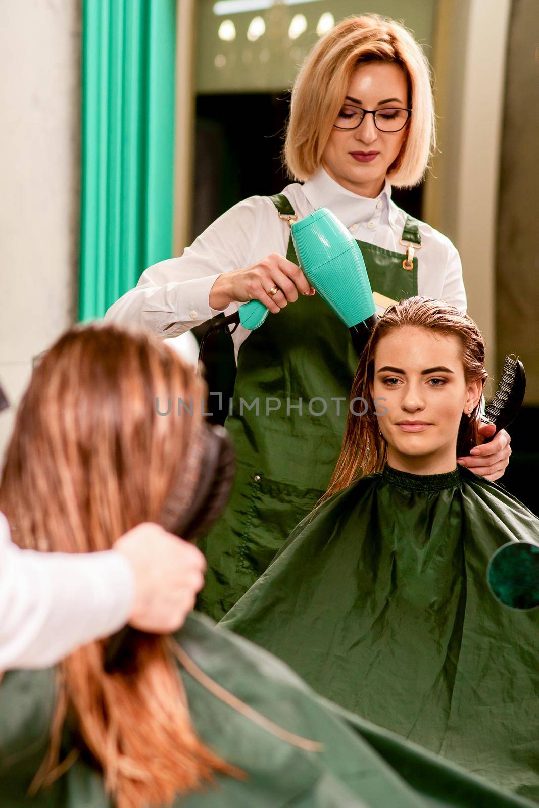 The hairdresser dries hair with a hairdryer of the beautiful young caucasian woman in the beauty salon. by okskukuruza