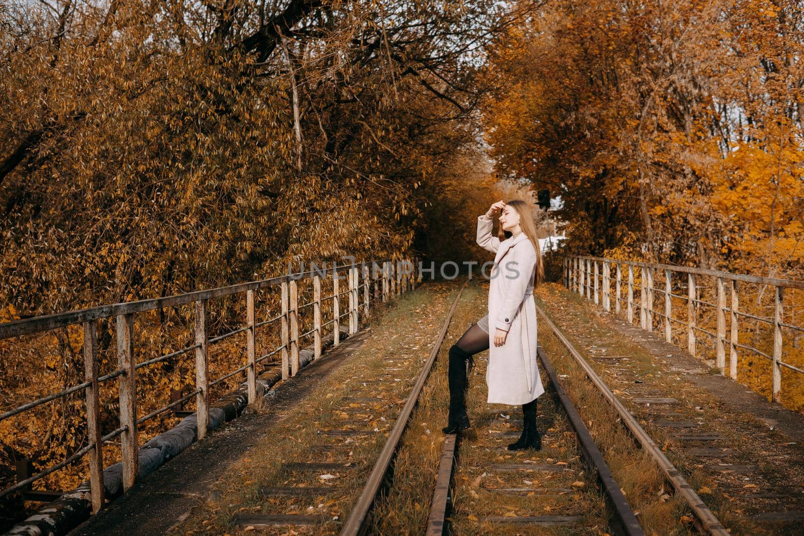 A beautiful long-haired woman walks through the autumn streets. Railway, autumn leaves, a woman in a light coat.