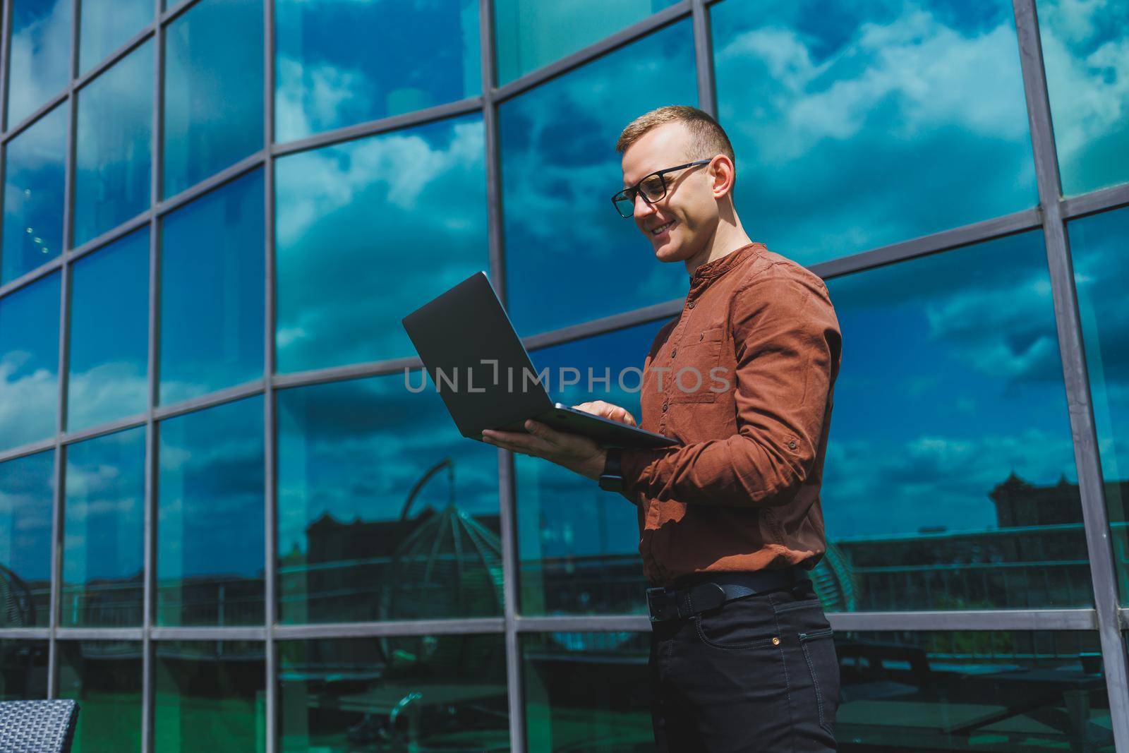 Cheerful businessman, formally dressed, pleased with received good news about contract details, sitting on office terrace with laptop, successful male entrepreneur