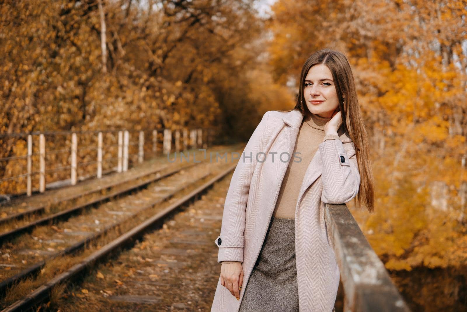 A beautiful long-haired woman walks through the autumn streets. Railway, autumn leaves, a woman in a light coat.