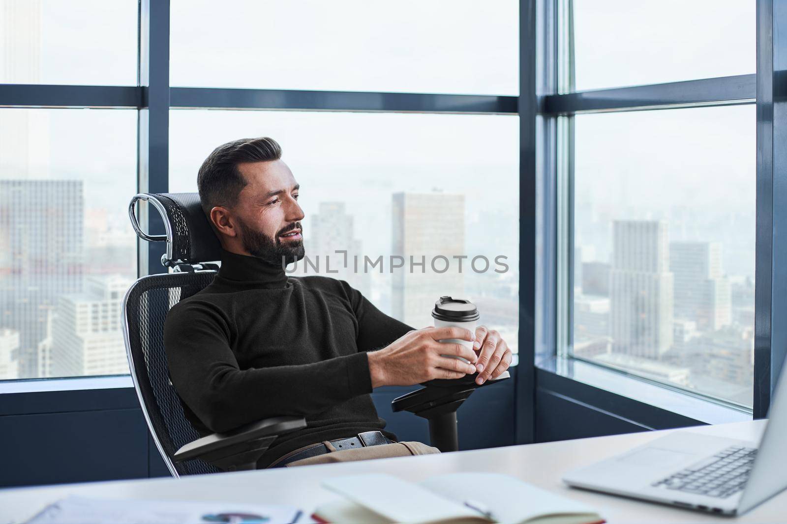 tired businessman drinks coffee sitting at his desk. by SmartPhotoLab