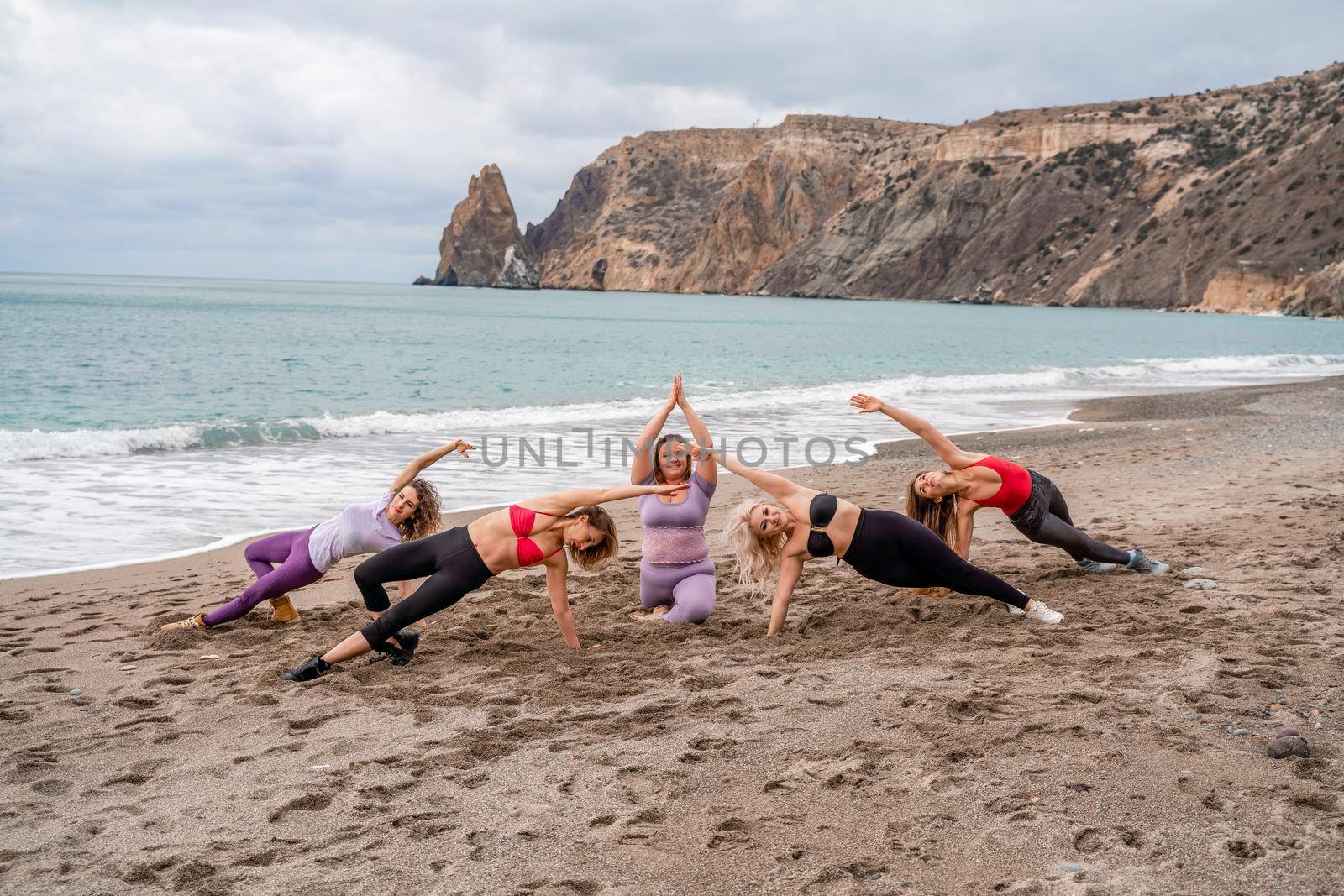 A group of five female friends are doing exercises on the beach. Beach holiday concept, healthy lifestyle by Matiunina