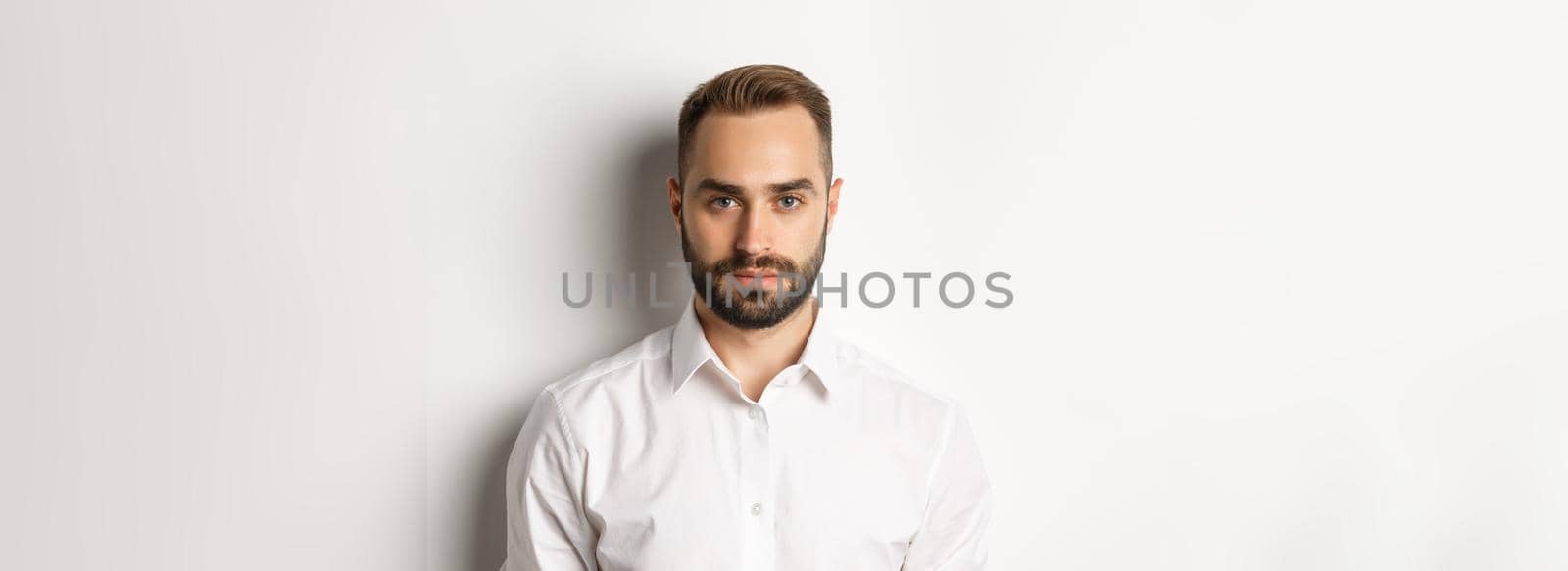 Close-up of serious businessman in white shirt looking at camera, standing confident by Benzoix