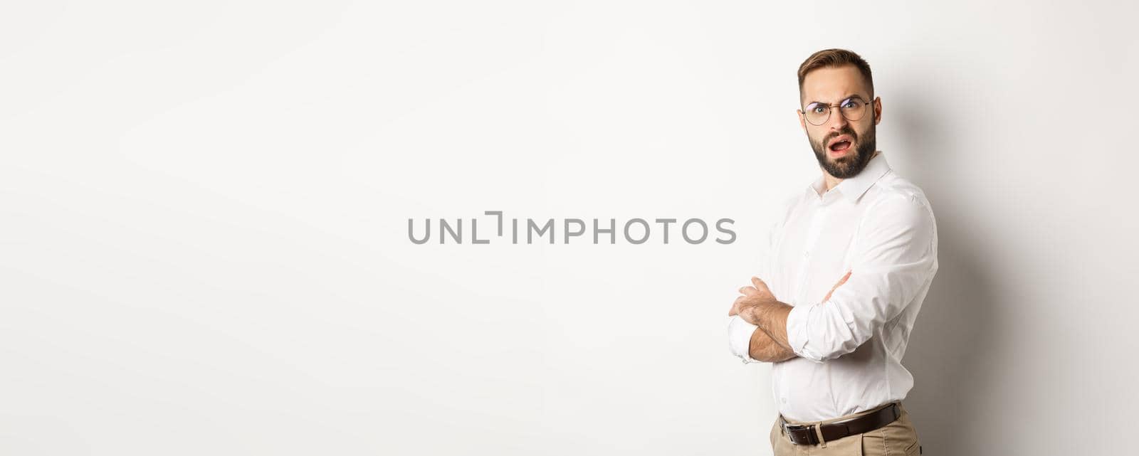 Confused manager looking at camera, standing shocked against white background.