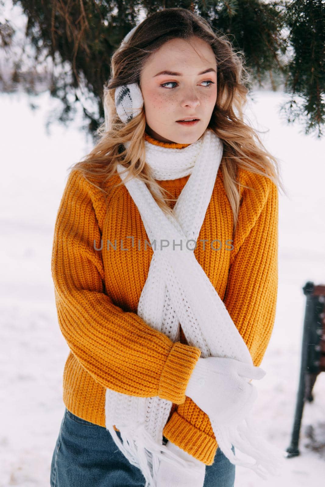 Teen blonde in a yellow sweater outside in winter. A teenage girl on a walk in winter clothes in a snowy forest.