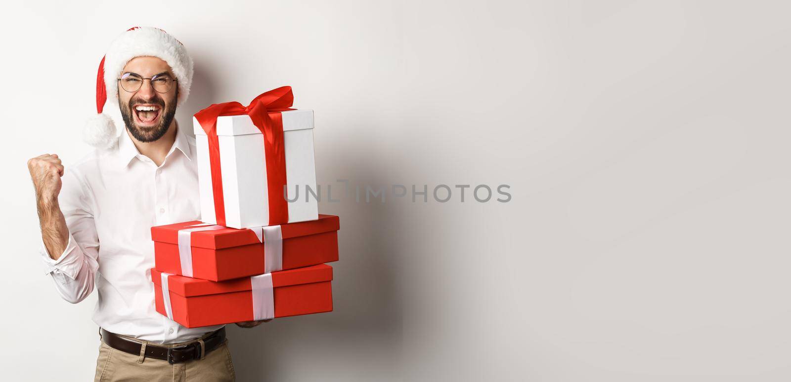 Merry christmas, holidays concept. Excited man receiving xmas gifts and rejoicing, wearing santa hat, celebrating New Year, white background by Benzoix
