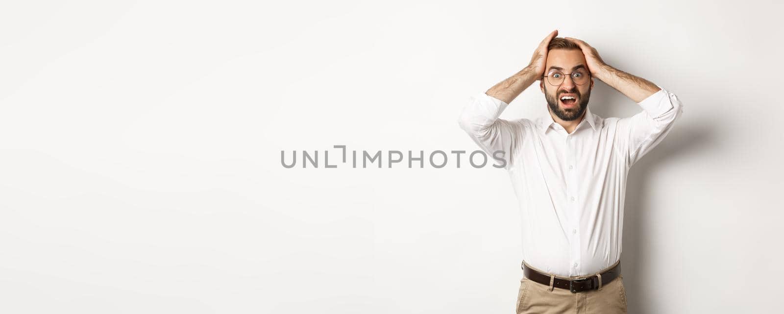 Frustrated businessman holding hands on head, looking shocked and anxious, standing over white background by Benzoix