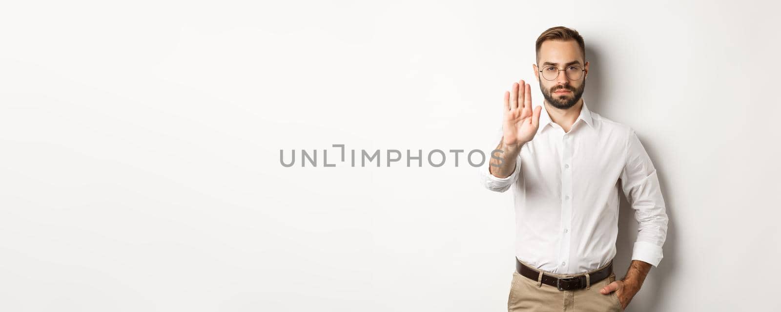 Serious boss in glasses showing stop sign, telling no, forbidding something, standing over white background.