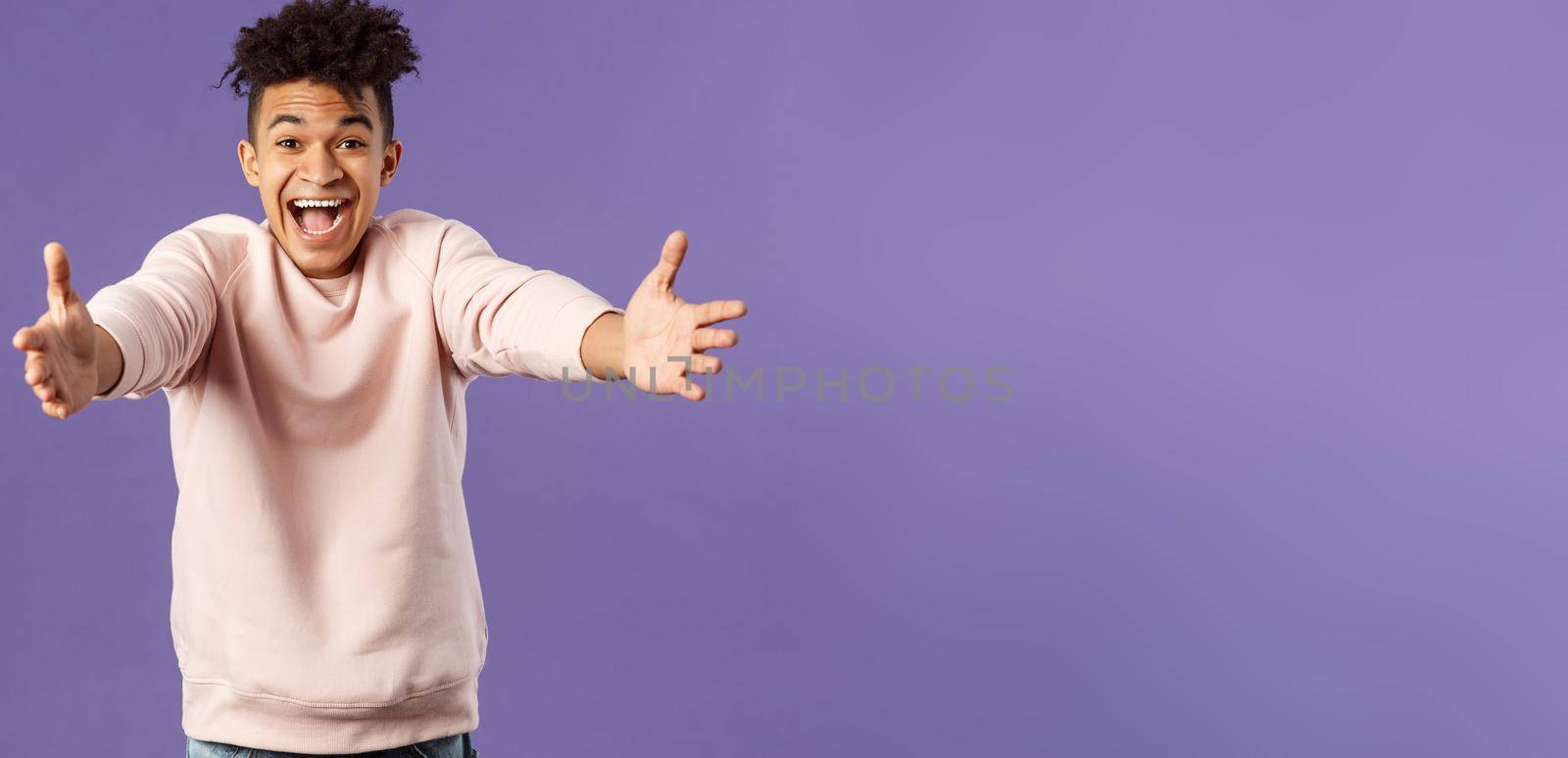 Portrait of happy charismatic, smiling hispanic man reaching hands to hug friend, laughing and grinning joyfully, meeting girlfriend at airport being cexcited finally see her, purple background.