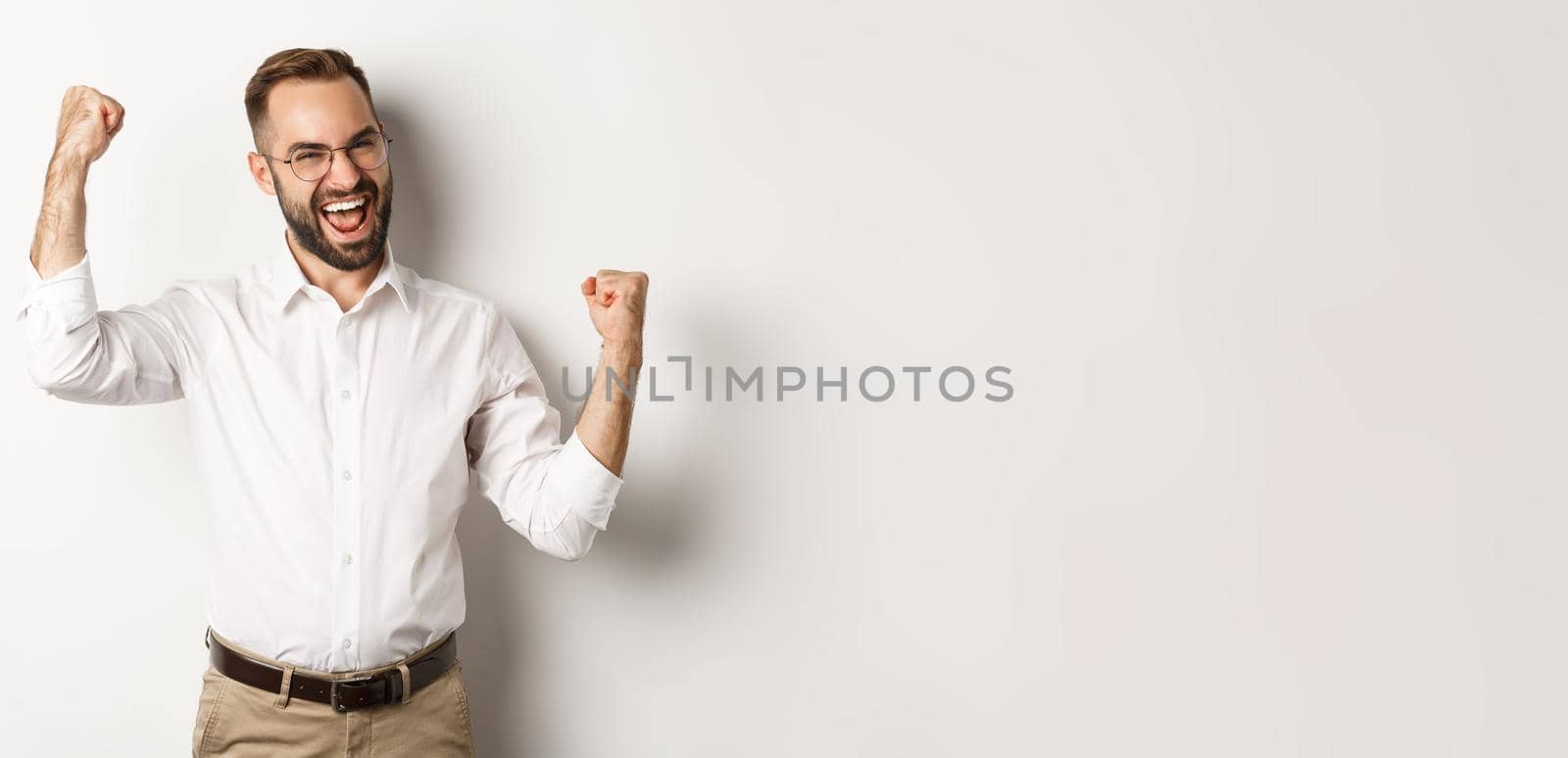 Successful businessman rejoicing, raising hands up and celebrating victory, winning something, standing over white background.