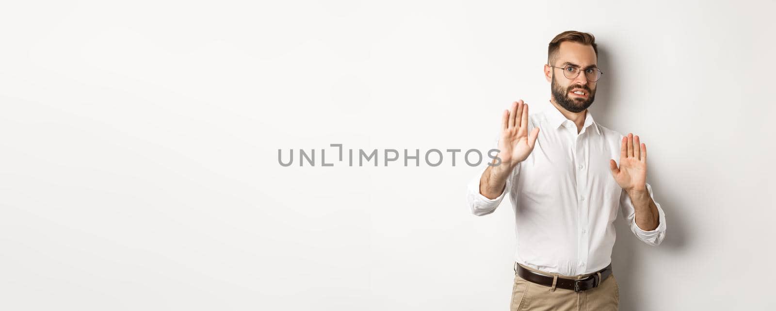 Displeased man rejecting something disturbing, showing stop sign and declining, cringe from aversion, standing over white background by Benzoix