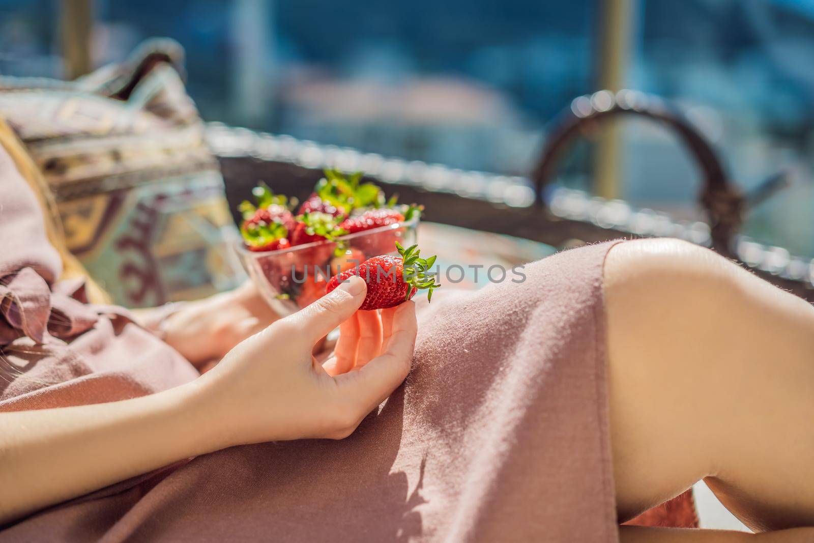 Portrait of gorgeous woman wearing beautiful dress sitting in a patio and eating strawberry.