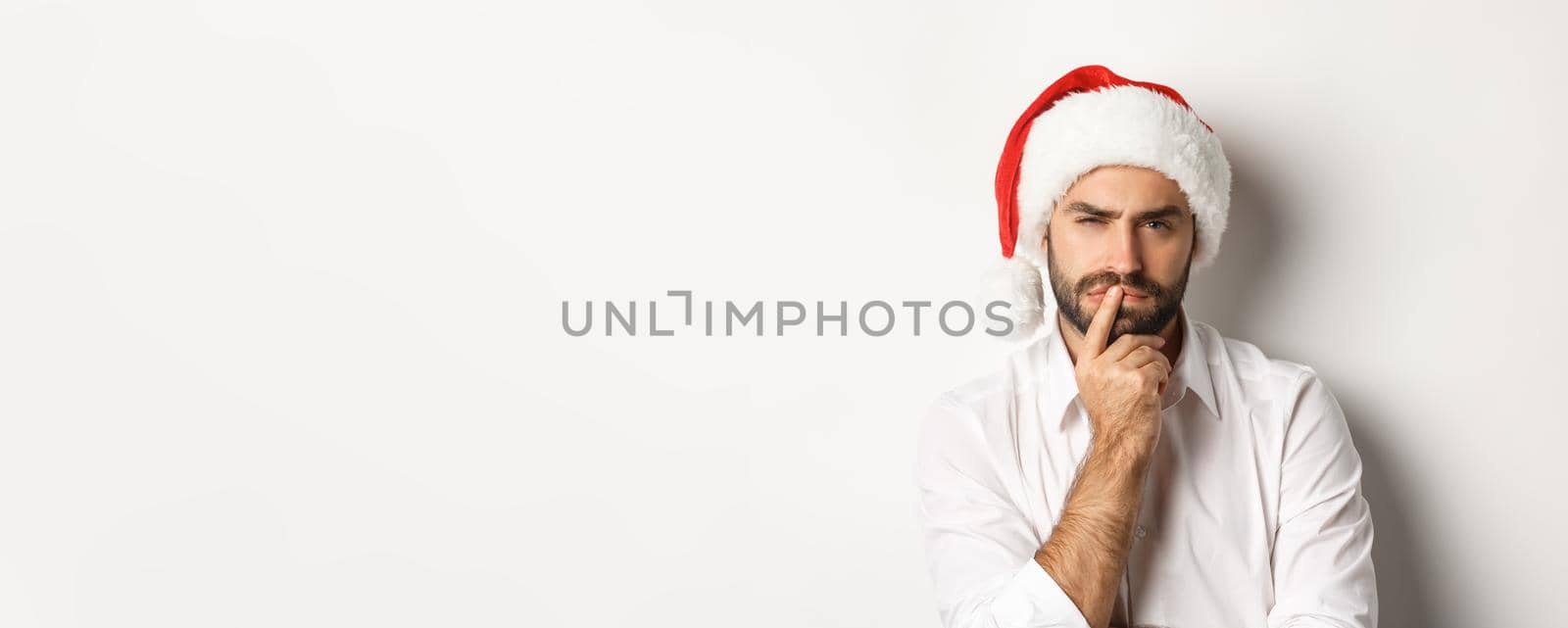 Party, winter holidays and celebration concept. Serious man thinking about christmas and new year, wearing santa hat, white background.