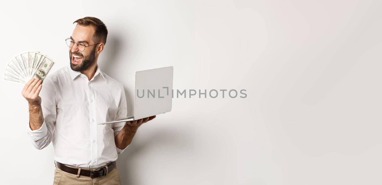 Business and e-commerce. Successful businessman using laptop for work and holding money, standing over white background by Benzoix