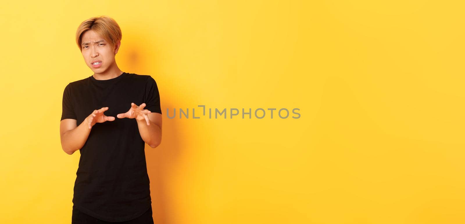 Portrait of disgusted picky asian guy, refusing and grimacing, standing yellow background by Benzoix