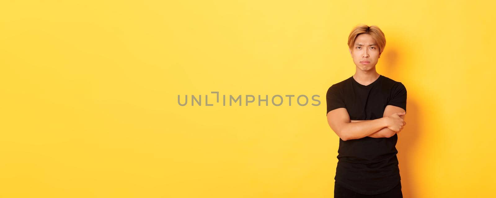 Worried serious-looking and concerned asian guy, cross arms chest and frowning at camera, yellow background by Benzoix