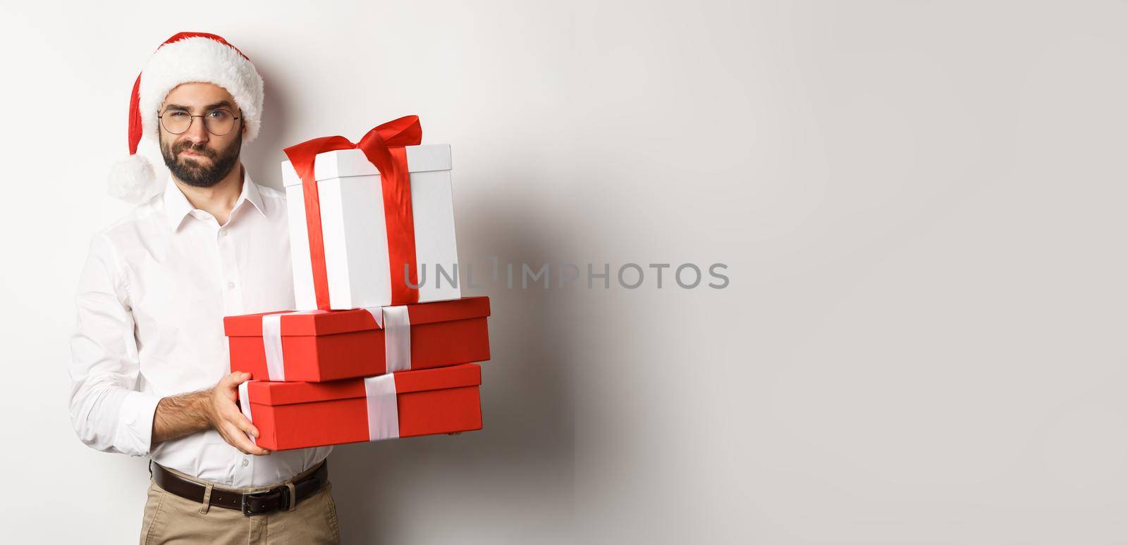 Merry christmas, holidays concept. Thoughtful man holding xmas gifts and looking suspicious at camera, celebrating New Year, white background by Benzoix