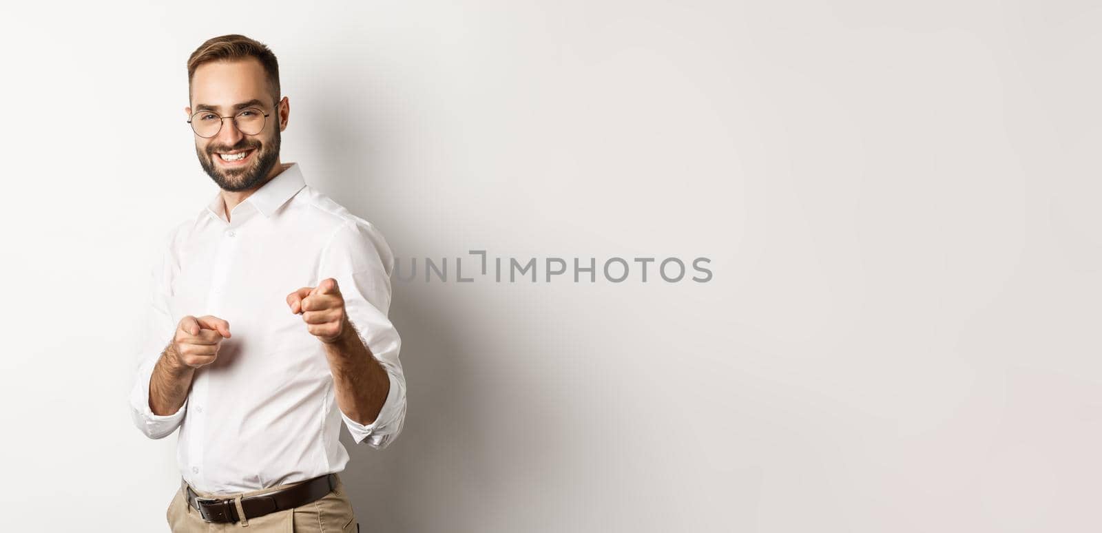 Confident businessman smiling, pointing fingers at you, congrats or praise gesture, standing over white background.