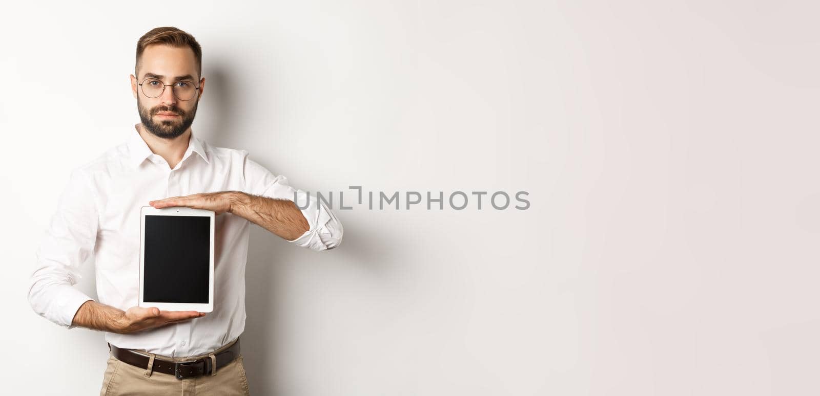Confident bearded man showing digital tablet screen, demonstrating app, standing over white background by Benzoix