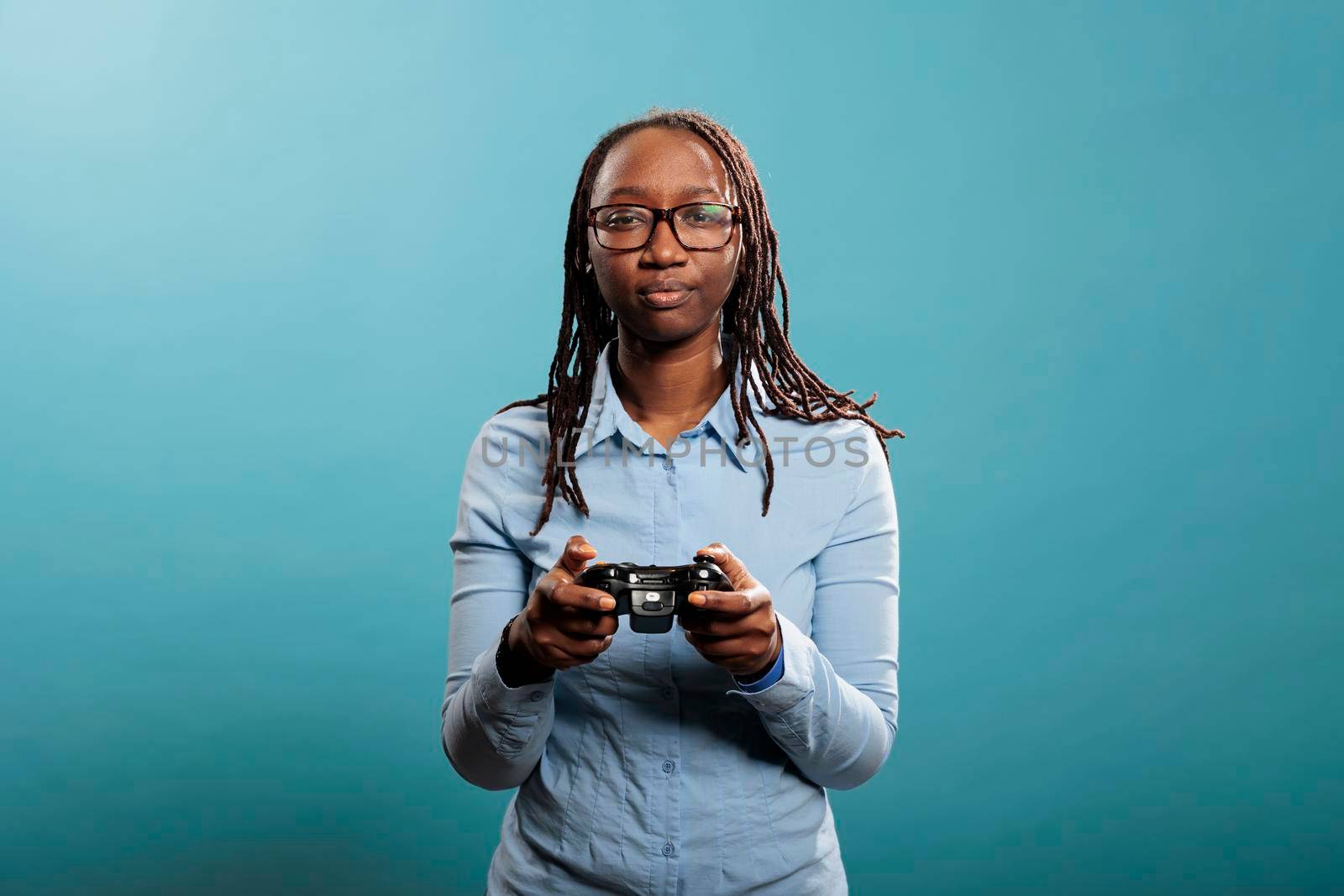 African american woman with modern console controller playing videogames on blue background. Young adult person enjoying competitive gaming while having gamepad. Studio shot.