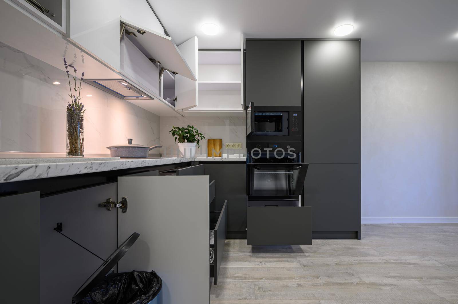 Showcase interior of modern simple dark grey and white kitchen, drawers retracted, doors open