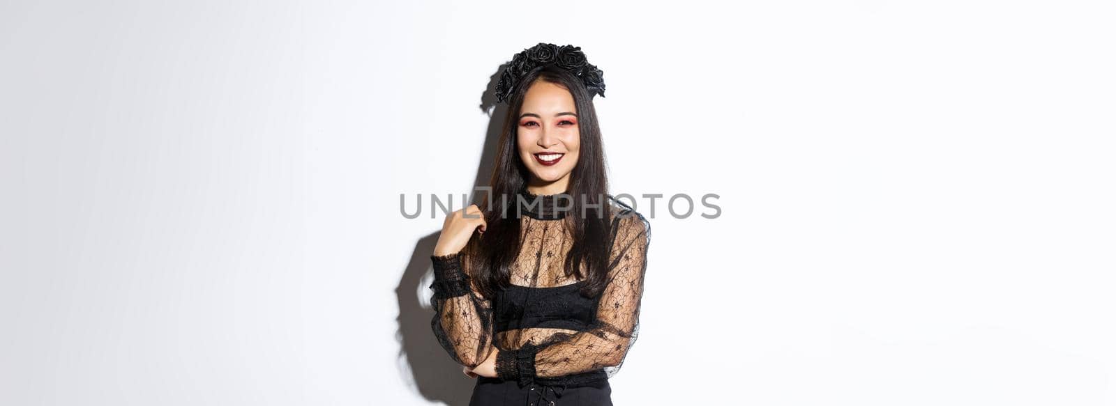 Beautiful young happy woman enjoying halloween party, smiling and looking cheerful while wearing her evil witch costume for trick or treating, standing over white background.
