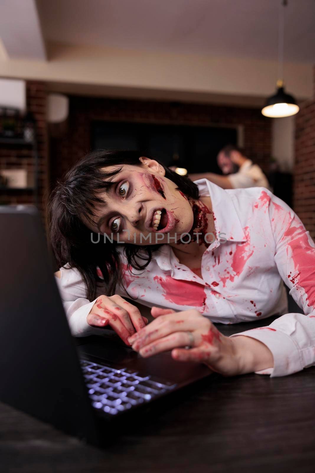 Scary horrific zombie using laptop at desk by DCStudio