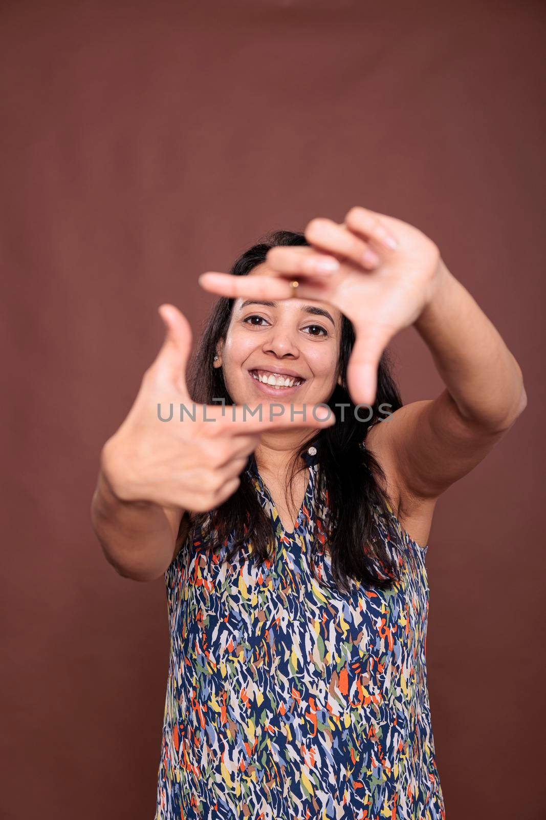 Smiling indian woman making photo frame gesture with fingers by DCStudio