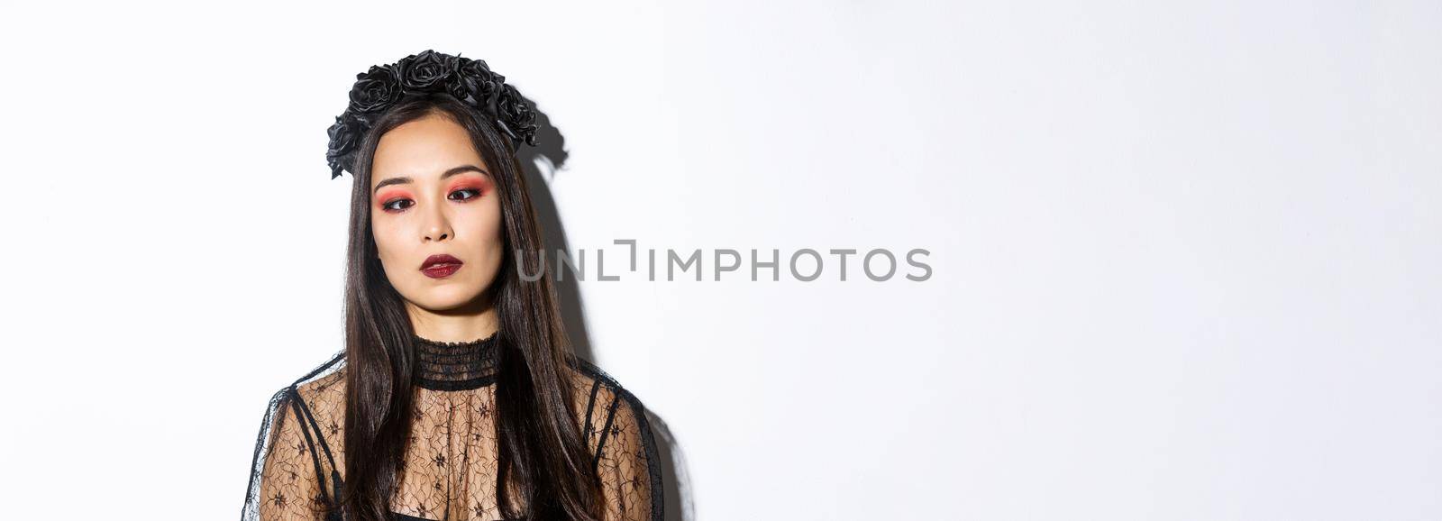 Close-up of bored and annoyed asian woman in halloween costume of witch squinting, trying to look at nose, standing over white background by Benzoix