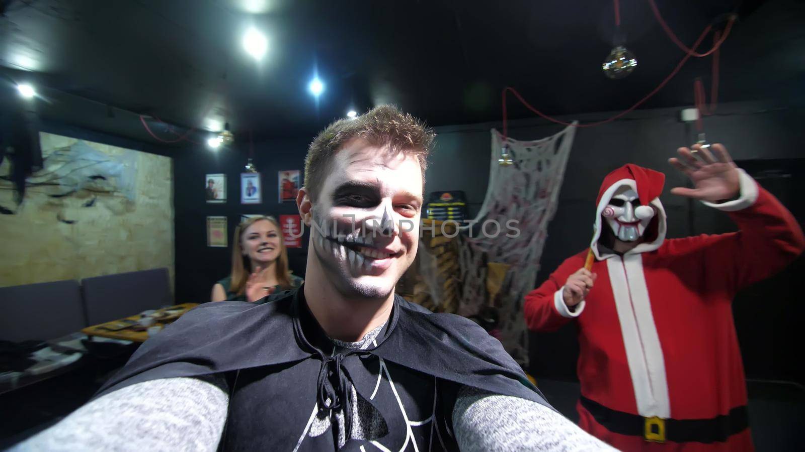 Halloween party, night, frightening portrait of a man with a terrible makeup in a black witch suit, croaks in front of the camera, in the background Halloween scenery is seen by djtreneryay