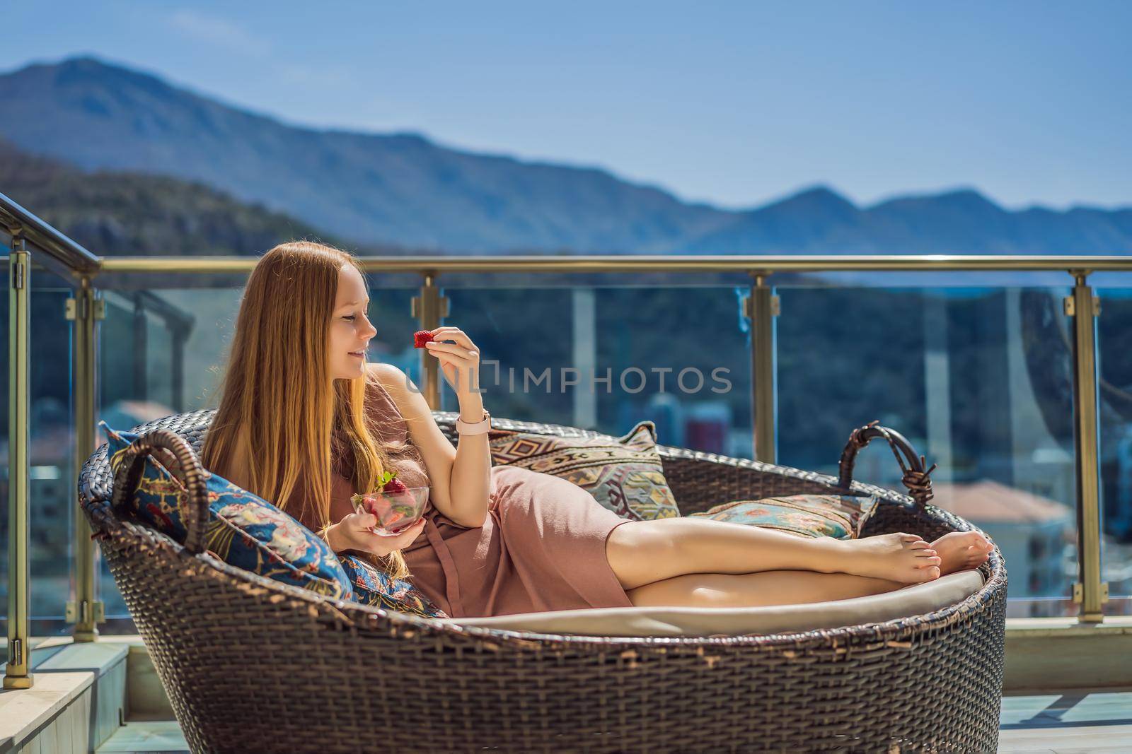 Portrait of gorgeous woman wearing beautiful dress sitting in a patio and eating strawberry.