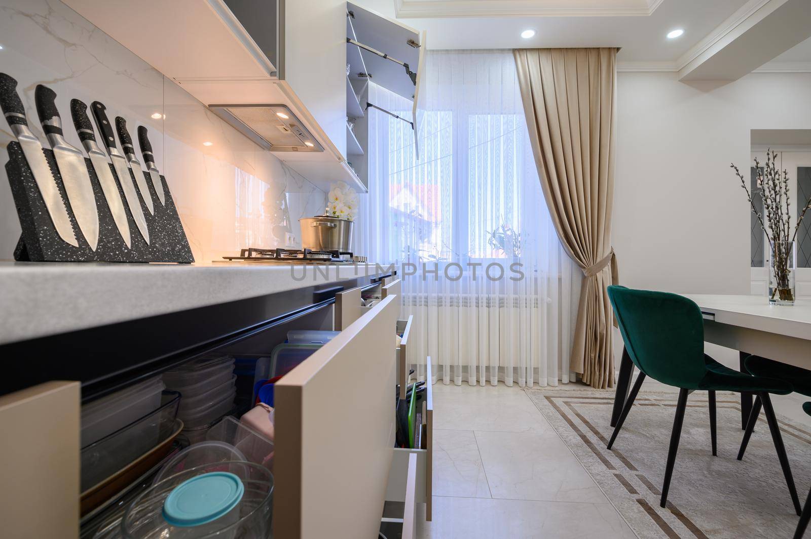 Details of modern white and beige luxurious kitchen in studio apartment interior, some drawers are open