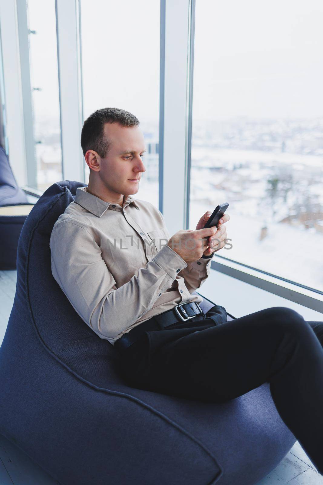 Successful male freelancer sitting in modern workspace and checking notifications on mobile phone in casual clothes. Remote work.