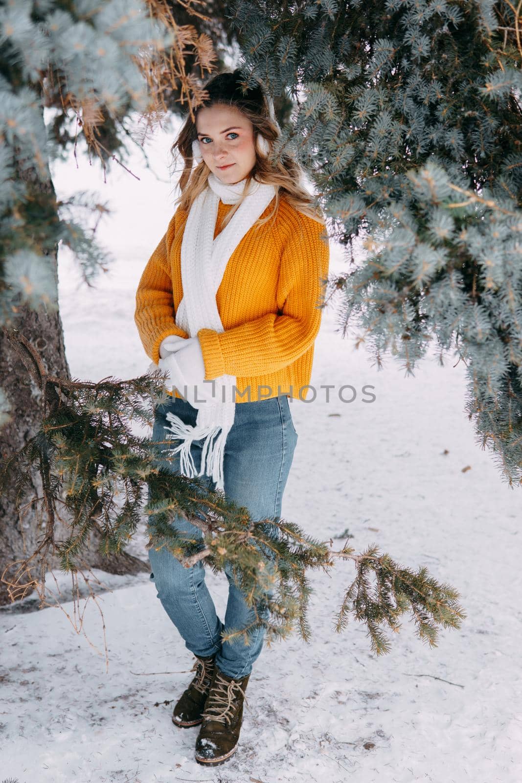 Teen blonde in a yellow sweater outside in winter. A teenage girl on a walk in winter clothes in a snowy forest.