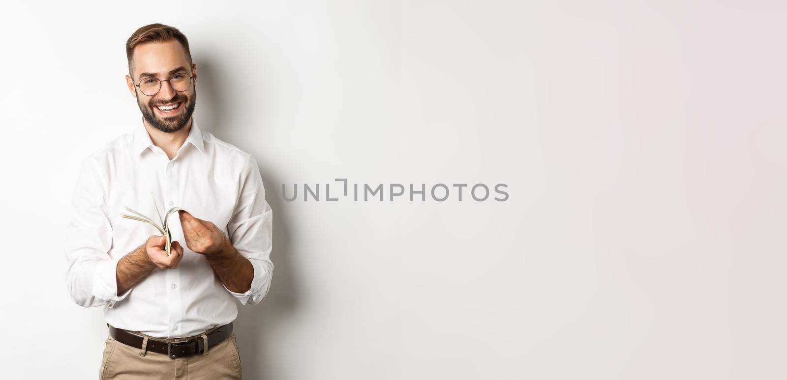 Successful businessman in white shirt, counting money and smiling satisfied, standing over white background.
