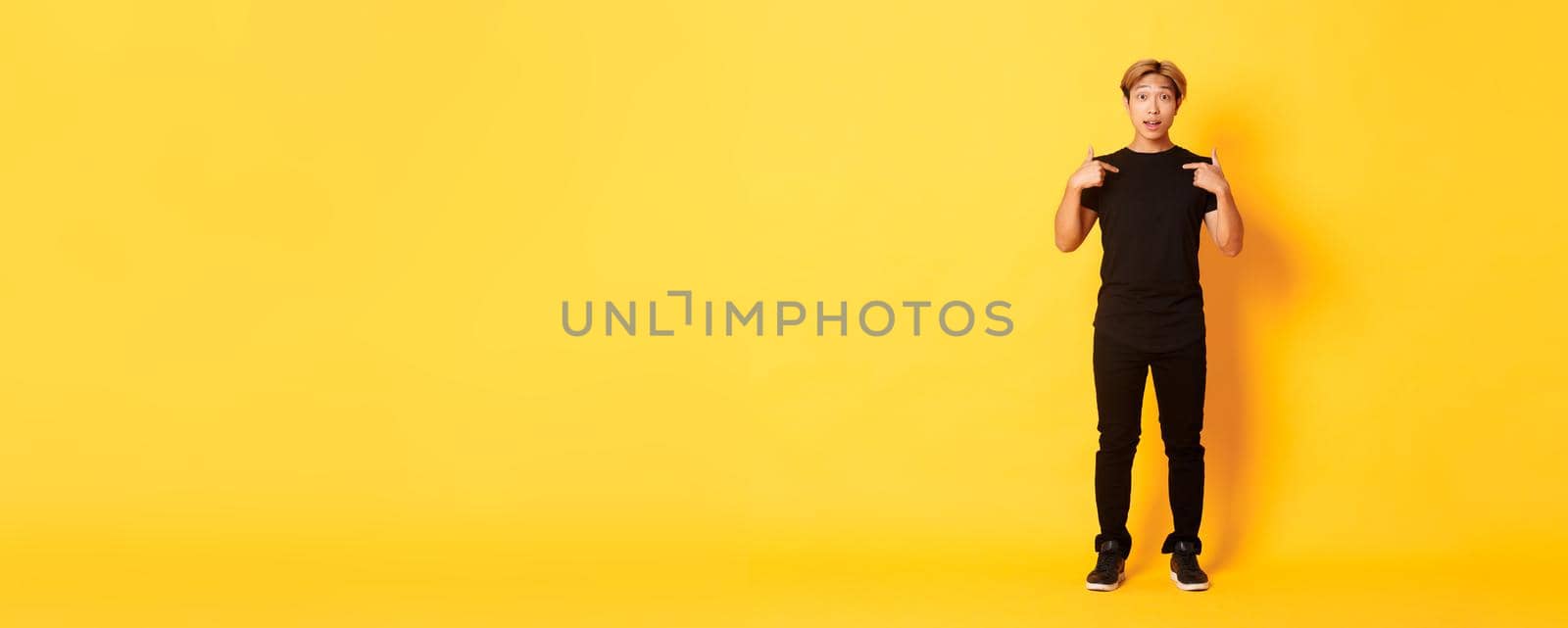 Full-length of surprised attractive korean blond guy in black outfit pointing at himself impressed, yellow background by Benzoix