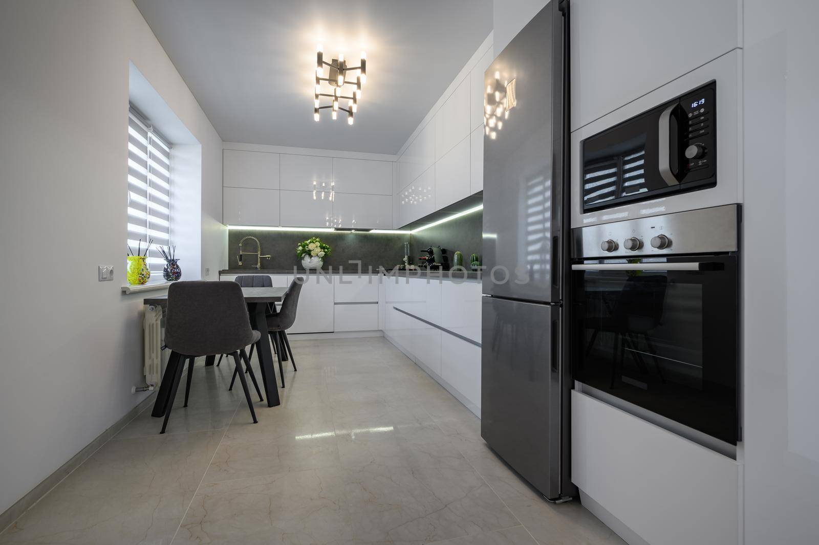 Luxurious modern trendy white and grey kitchen interior after renovation, with granite counter top and marble floor, dining table next to window