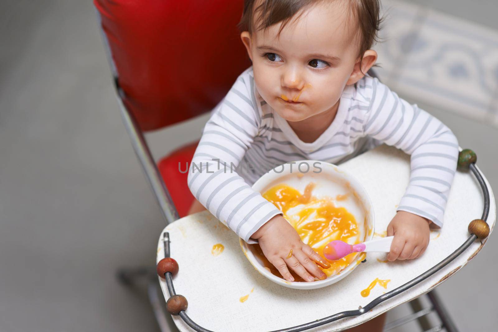 Im still a bit peckish. a cute little baby sitting in a high chair eating