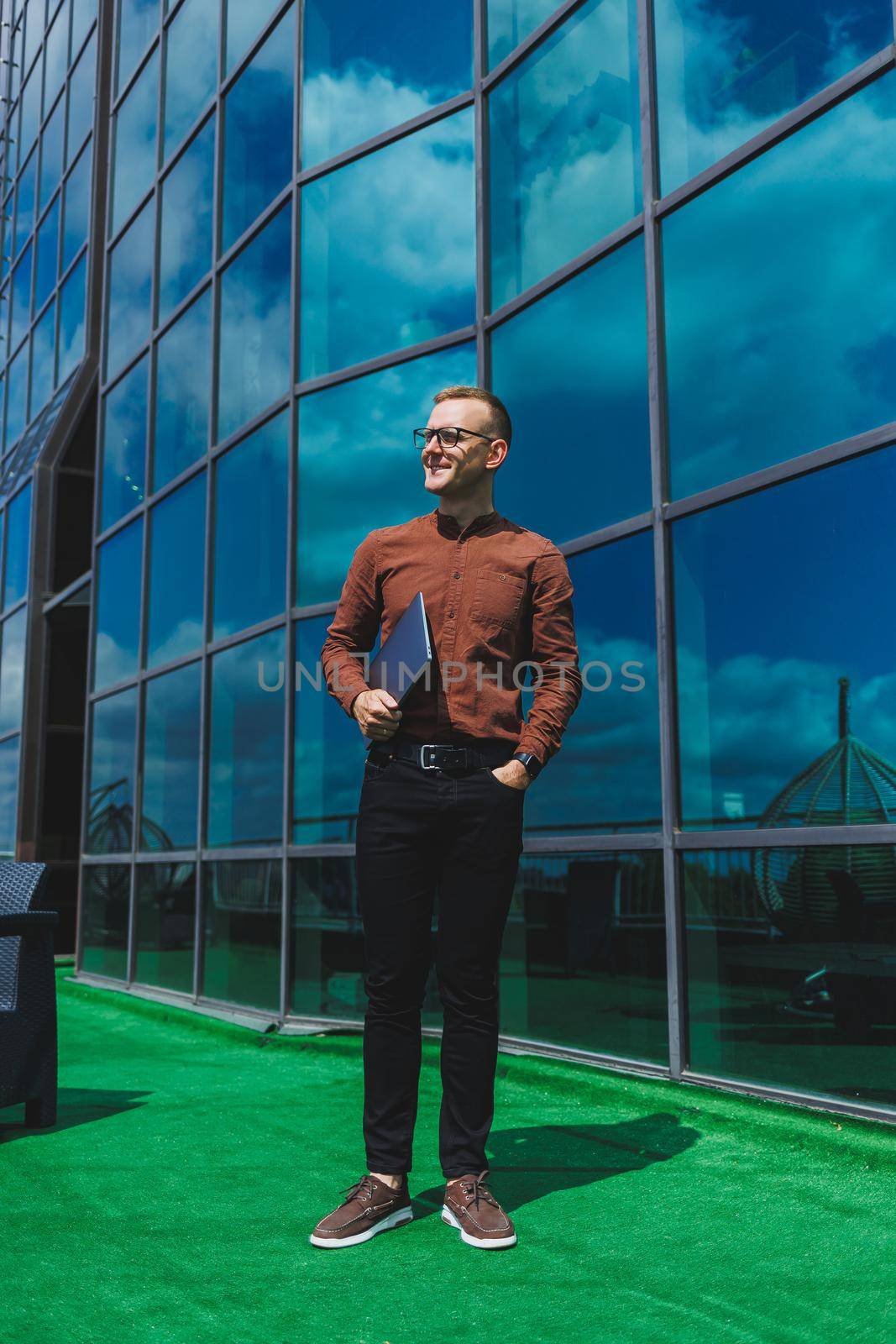 Cheerful businessman, formally dressed, pleased with received good news about contract details, sitting on office terrace with laptop, successful male entrepreneur