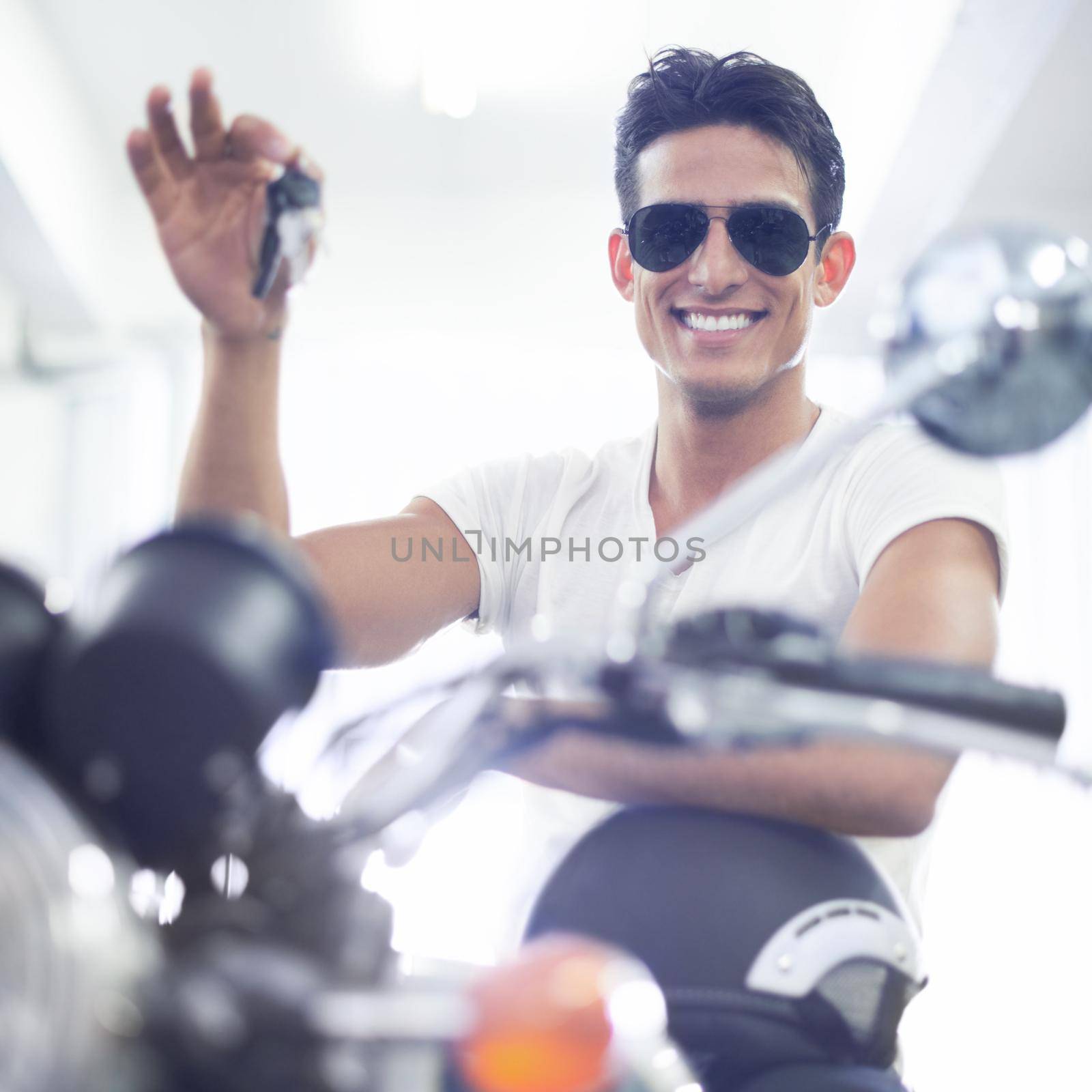 Ready for some fun. A handsome young man sitting on his motorcycle while holding its keys. by YuriArcurs