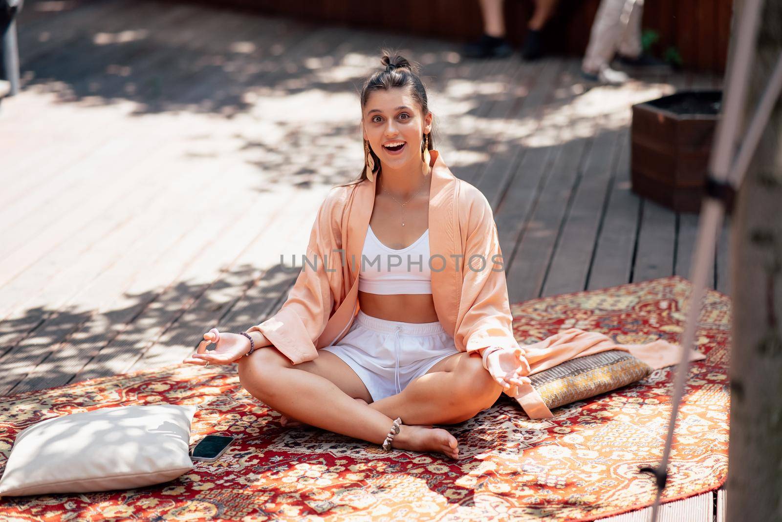 Young woman is practising yoga sitting on a wooden podium in the garden in the sunny morning