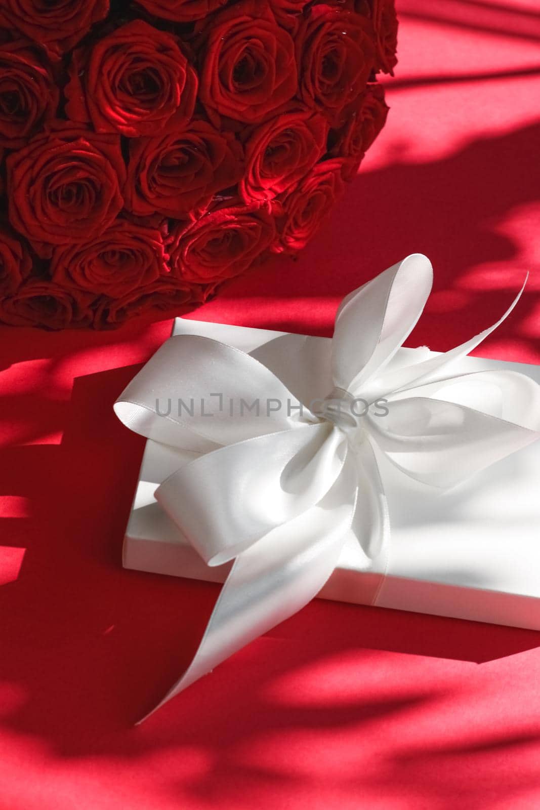 Happy holidays, luxe shopping and love gifts concept - Luxury holiday silk gift box and bouquet of roses on red background, romantic surprise and flowers as birthday or Valentines Day present