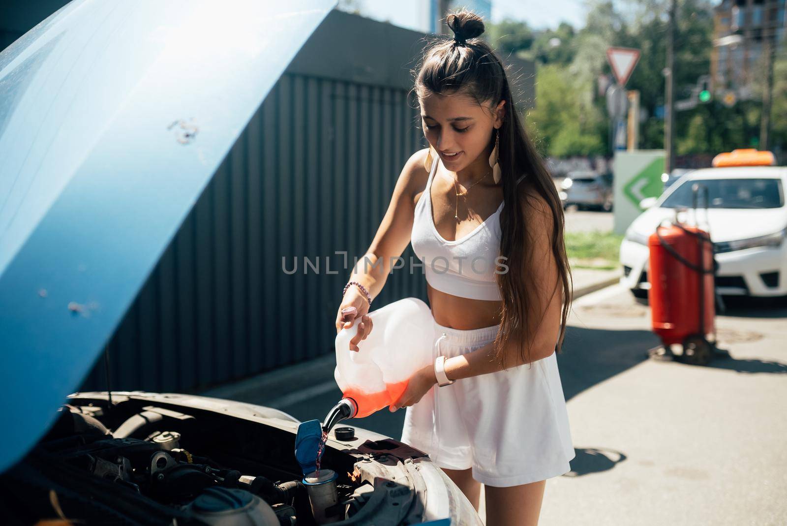 Young woman pouring antifreeze car screen wash liquid into car by teksomolika