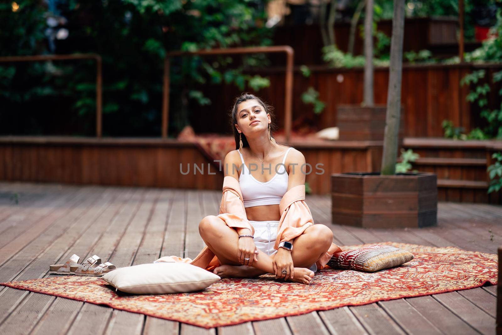 Young woman is practising yoga sitting on a wooden podium in the garden in the sunny morning