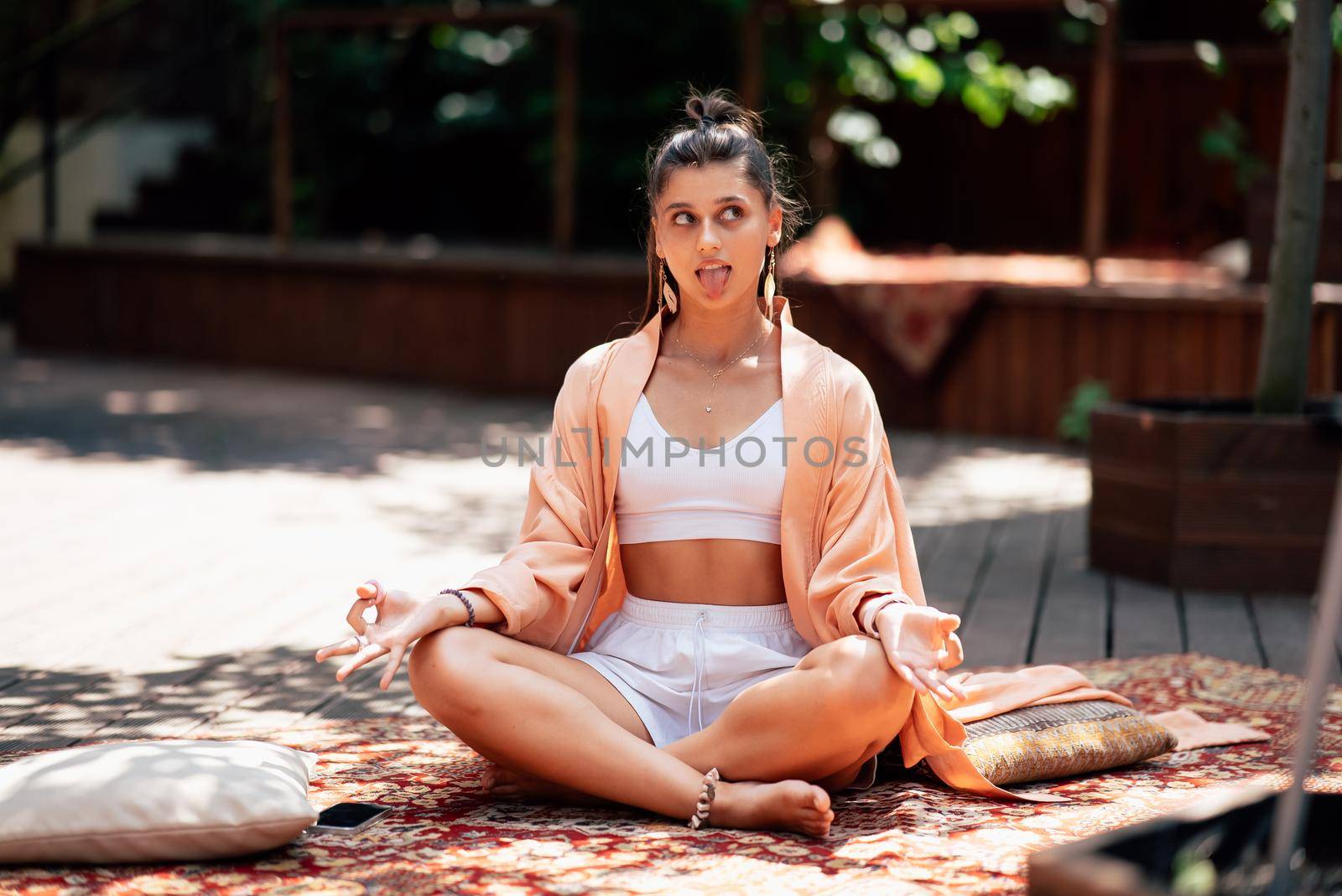 Young woman is practising yoga sitting on a wooden podium in the garden in the sunny morning