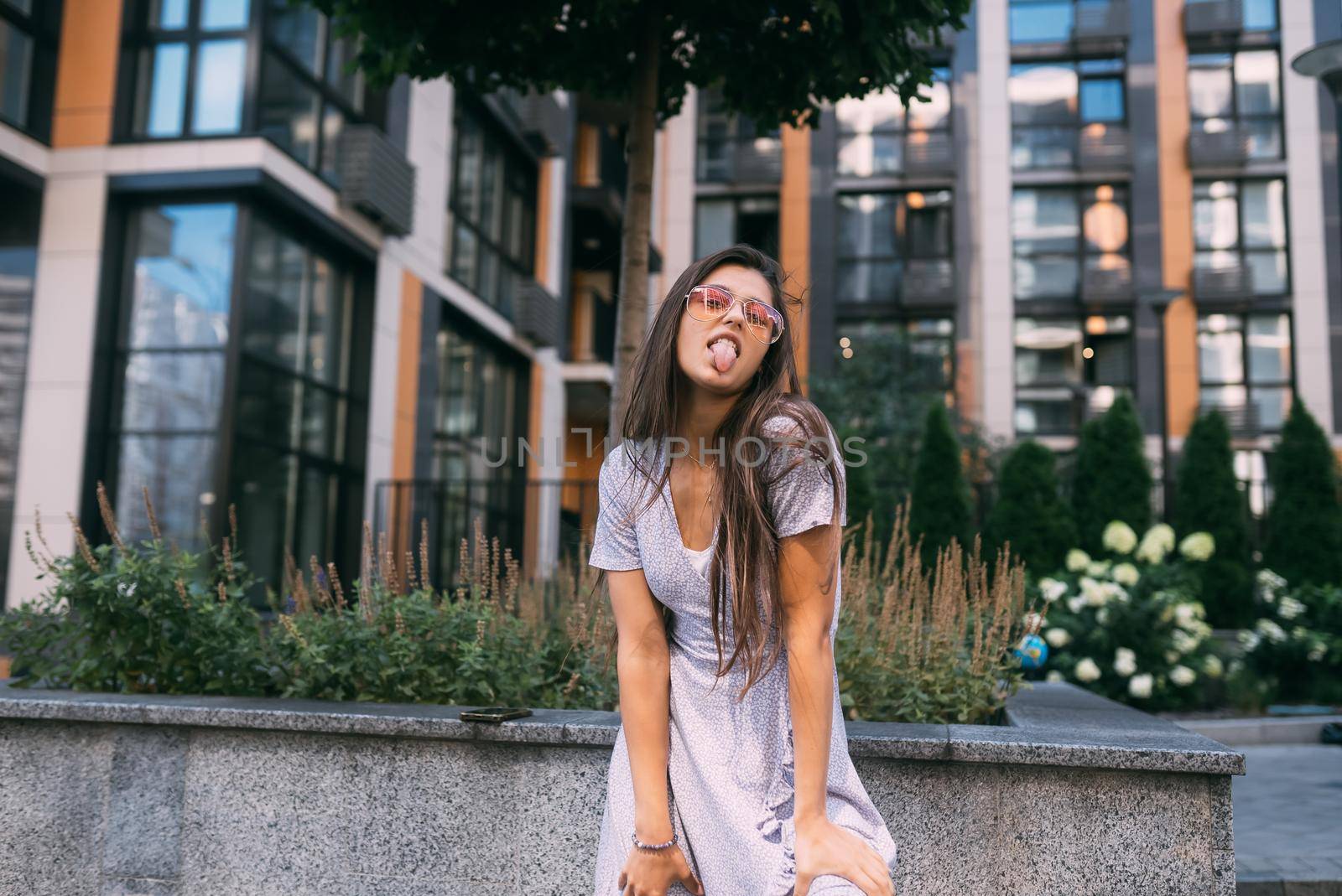 Summer time. Happy cheerful girl laughs on the background of large building in city.