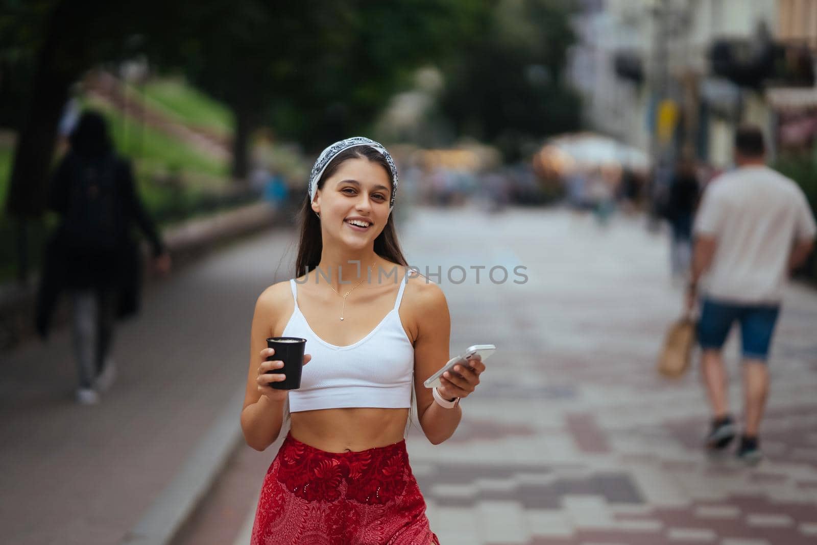 Cheerful woman in the street drinking morning coffee and use her smartphone. Young woman using phone on the street.