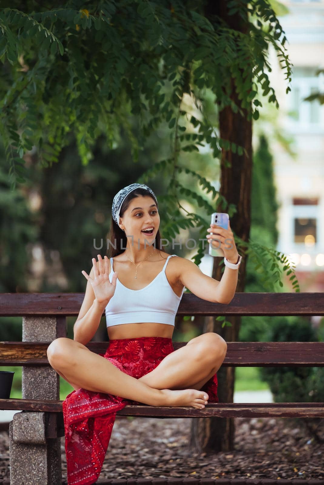 Happy girl using a smartphone in a city park sitting on a bench