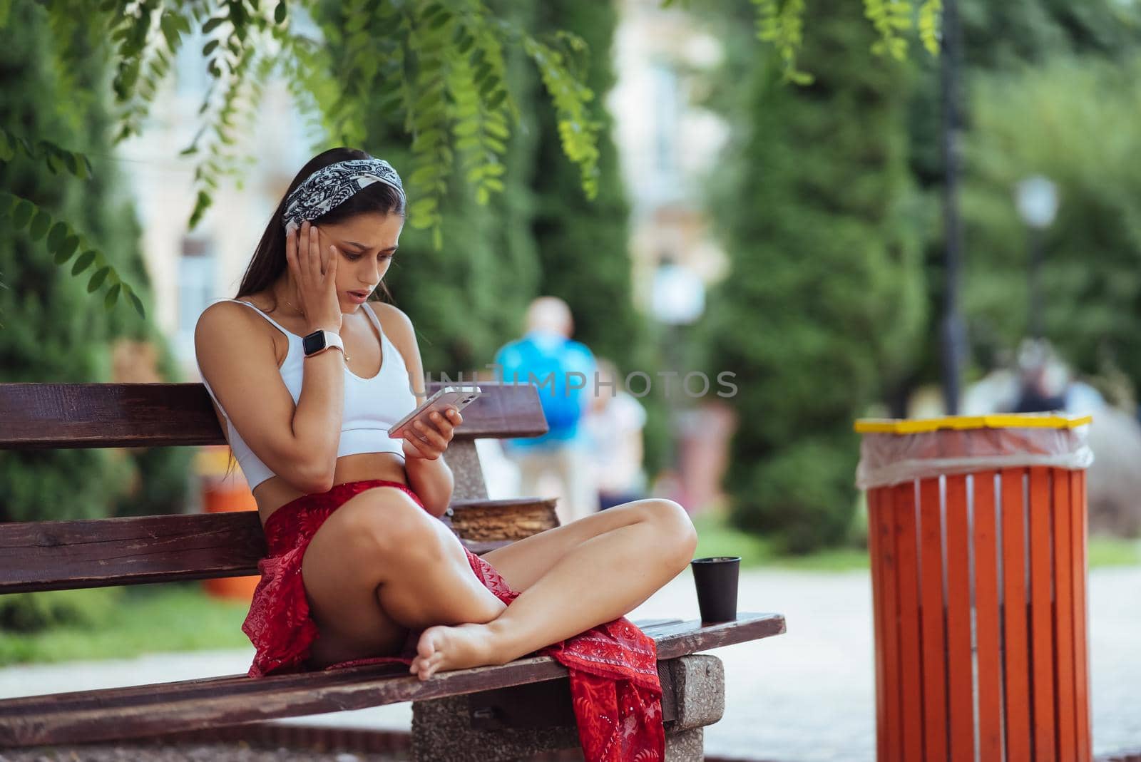 Happy girl using a smartphone in a city park sitting on a bench